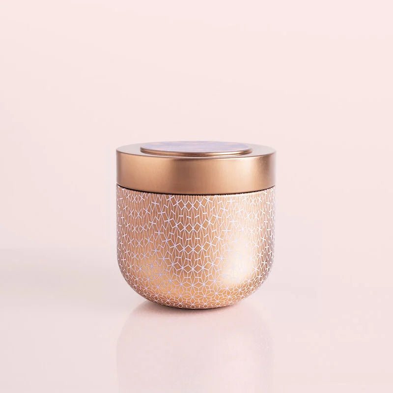 A round gilded tin jar with a textured geometric pattern and matching flat lid, the Capri BLUE Pink Grapefruit & Prosecco 12.5 oz Candle sits against a pale neutral background.