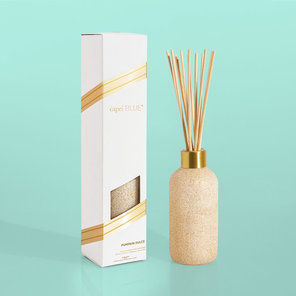 Set against a turquoise background, the Capri BLUE Pumpkin Dulce 8oz Reed Diffuser exudes an inviting autumn fragrance. It features a textured tan bottle with reeds and a white box adorned with gold accents, making it the perfect holiday gift.