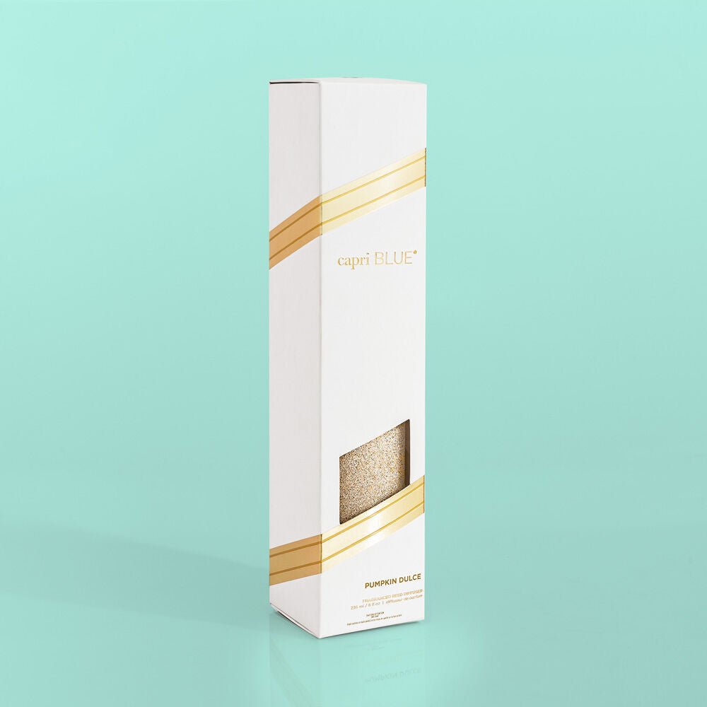 A tall white and gold box reads Capri BLUE and Pumpkin Dulce 8oz Reed Diffuser against a teal backdrop. A small window previews the product, making it an ideal holiday gift that captures the essence of autumn fragrance.