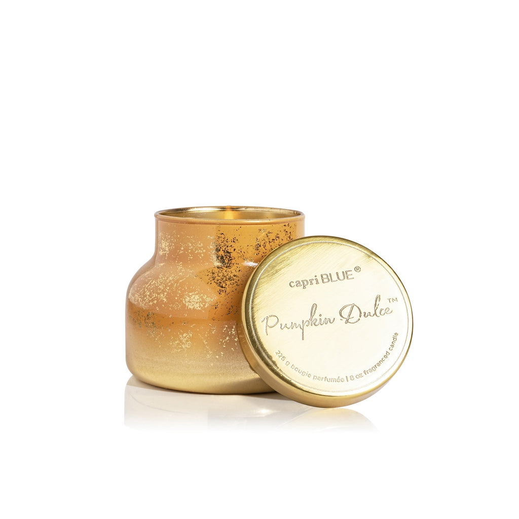 A gold, speckled Capri BLUE Pumpkin Dulce Petite Jar candle (8 oz) with a lid rests nearby. Its short, wide shape features a metallic shine and decorative texture, perfect for the holidays.