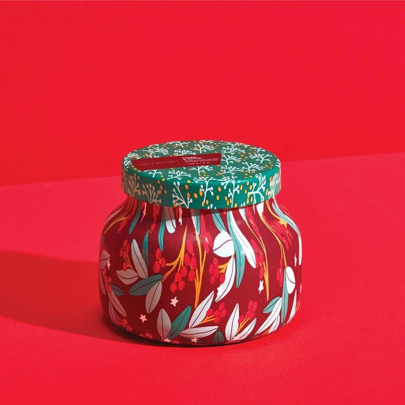 The Capri BLUE - Tinsel & Spice Holiday Pattern Play Signature Jar 8 oz Candle features festive red, green, and white floral and leaf designs on a bright red background. With a coordinating green lid, its ideal for the holiday season while doubling as both decor and candle.