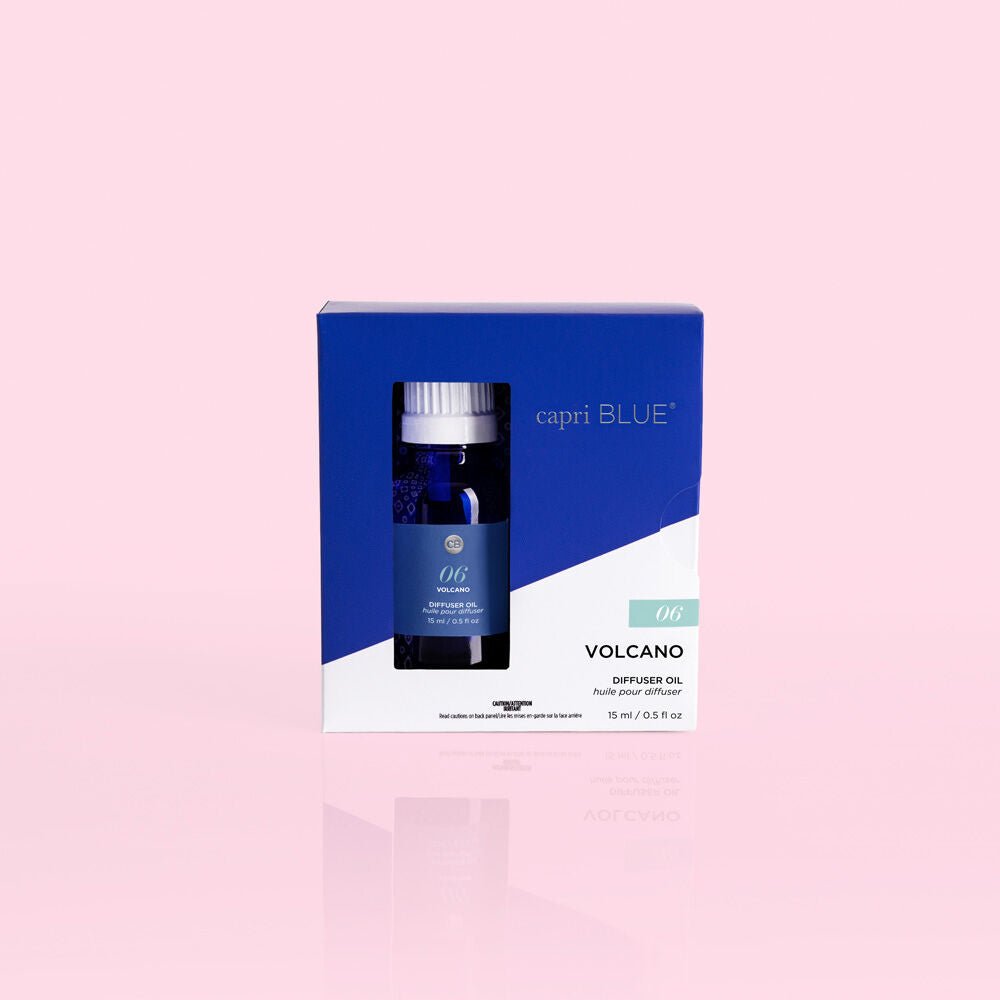 A blue and white box housing the Capri BLUE - Volcano 0.5oz Diffuser Oil showcases sugared citrus essence. The minimalist packaging against a pink backdrop partially reveals the bottle through a transparent window.