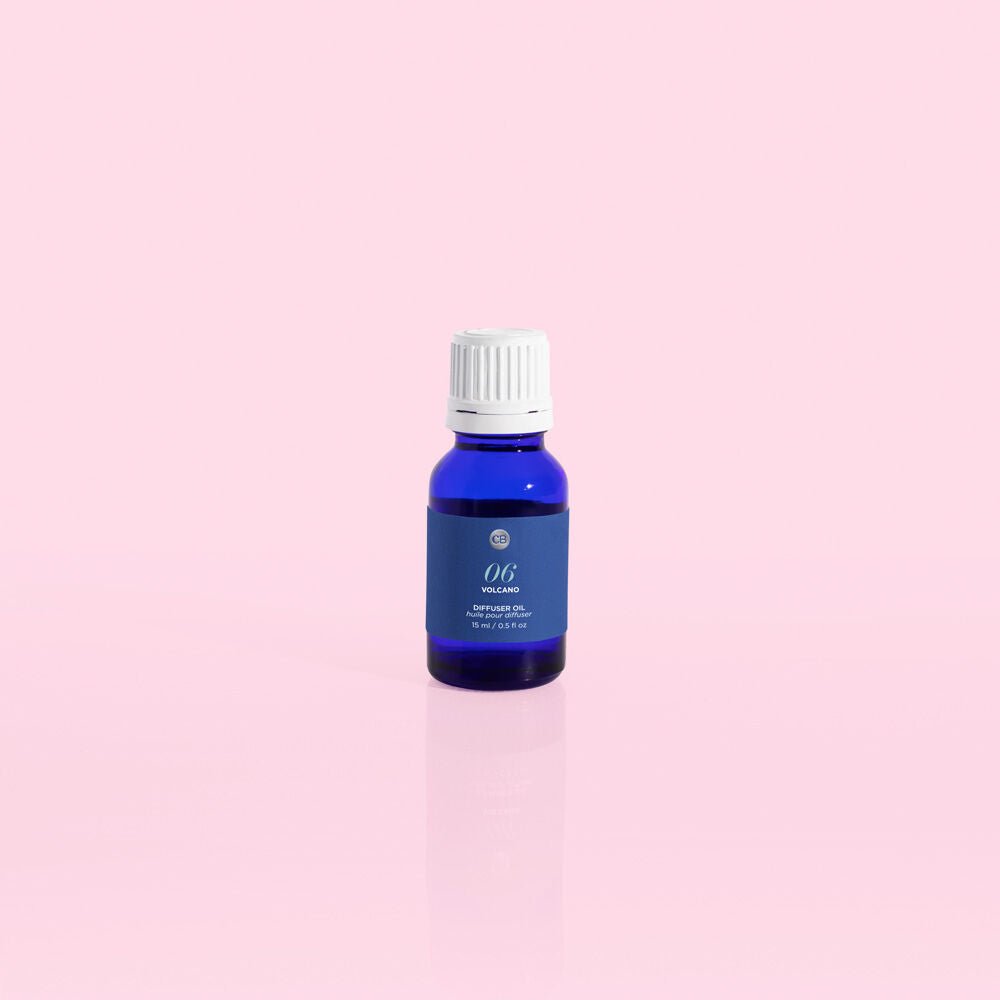 A small blue bottle with a white cap, set against a pastel pink background, evokes the refreshing scent of Capri BLUE - Volcano 0.5oz Diffuser Oil. Its label hints at sugared citrus aromas but keeps specifics intriguingly vague.