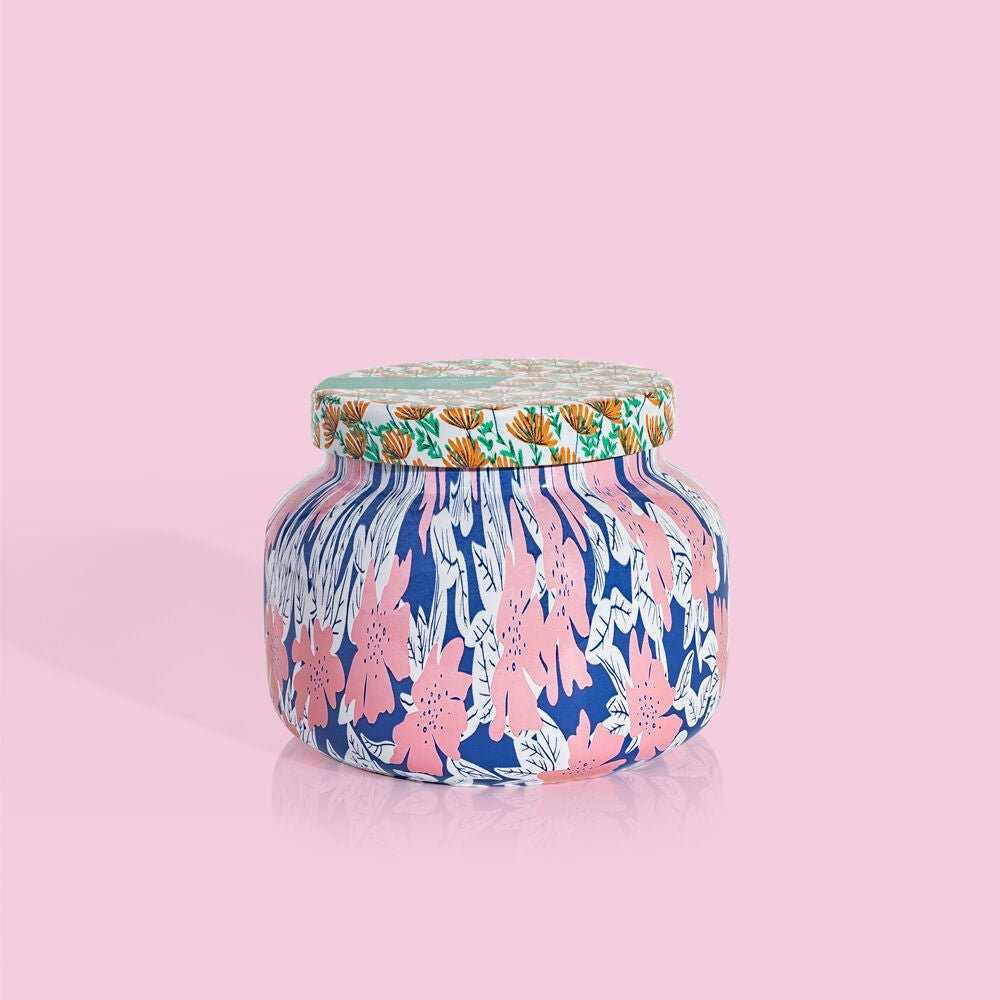 The Capri BLUE Volcano 19oz Pattern Play Signature Jar Candle features a colorful floral design in pink, blue, white, and orange—ideal for a vibrant décor accent—presented against a solid light pink background.