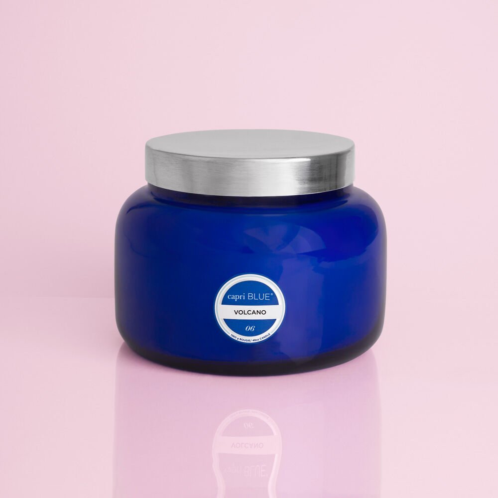 The Capri BLUE - Volcano 48oz Blue Jumbo Jar Candle, featuring sugared citrus and tropical fruits, with a silver lid and white label, is displayed against a pink background.
