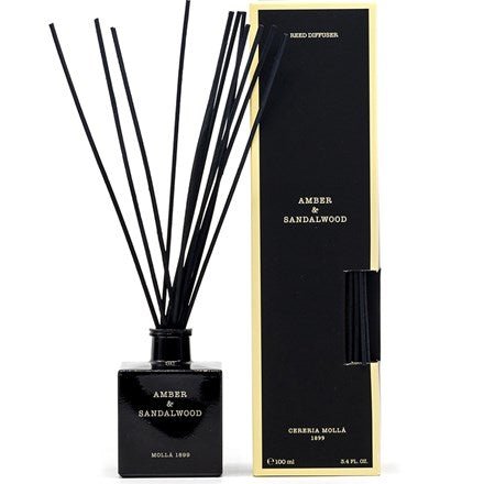 The Cereria Molla Amber & Sandalwood 3.4oz reed diffuser features a chic black bottle with rattan rods and an elegant label, accompanied by a matching box with gold trim.