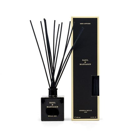 A Cereria Molla Basil & Mandarin Reed Diffuser, featuring a square black glass bottle and black reeds, stands beside its matching box with yellow trim, filling the air with refreshing citrus notes.