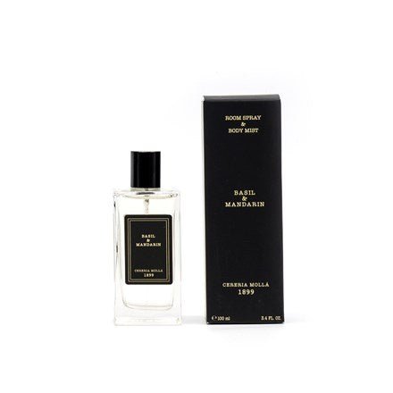 The Cereria Molla Basil & Mandarin 3.4oz Room Spray & Body Mist, with its citrus fragrance, comes in a clear bottle with a black label and cap, perfectly complemented by its sleek black box adorned with gold lettering, all elegantly set against a crisp white background.