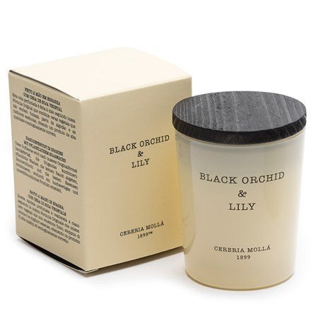 The Cereria Molla Black Orchid & Lily 2.47oz Candle is crafted from vegetable wax, featuring a black wooden lid and a white label with its name. It sits beside a cream-colored box, adorned with elegant black text for sophistication.