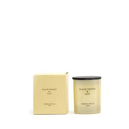 A handmade Cereria Molla - Black Orchid & Lily 8oz candle in a cream glass container sits beside its matching box. The minimalist design features understated black text with Cereria Molla elegantly displayed, both items sharing the same cream and black color scheme.