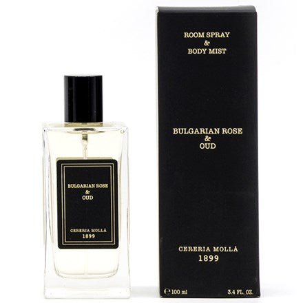 A 3.4oz rectangular bottle of Cereria Molla - Bulgarian Rose & Oud Room Spray & Body Mist has a black cap and is paired with a stylish black box featuring gold text, offering an exquisite fragrance experience.