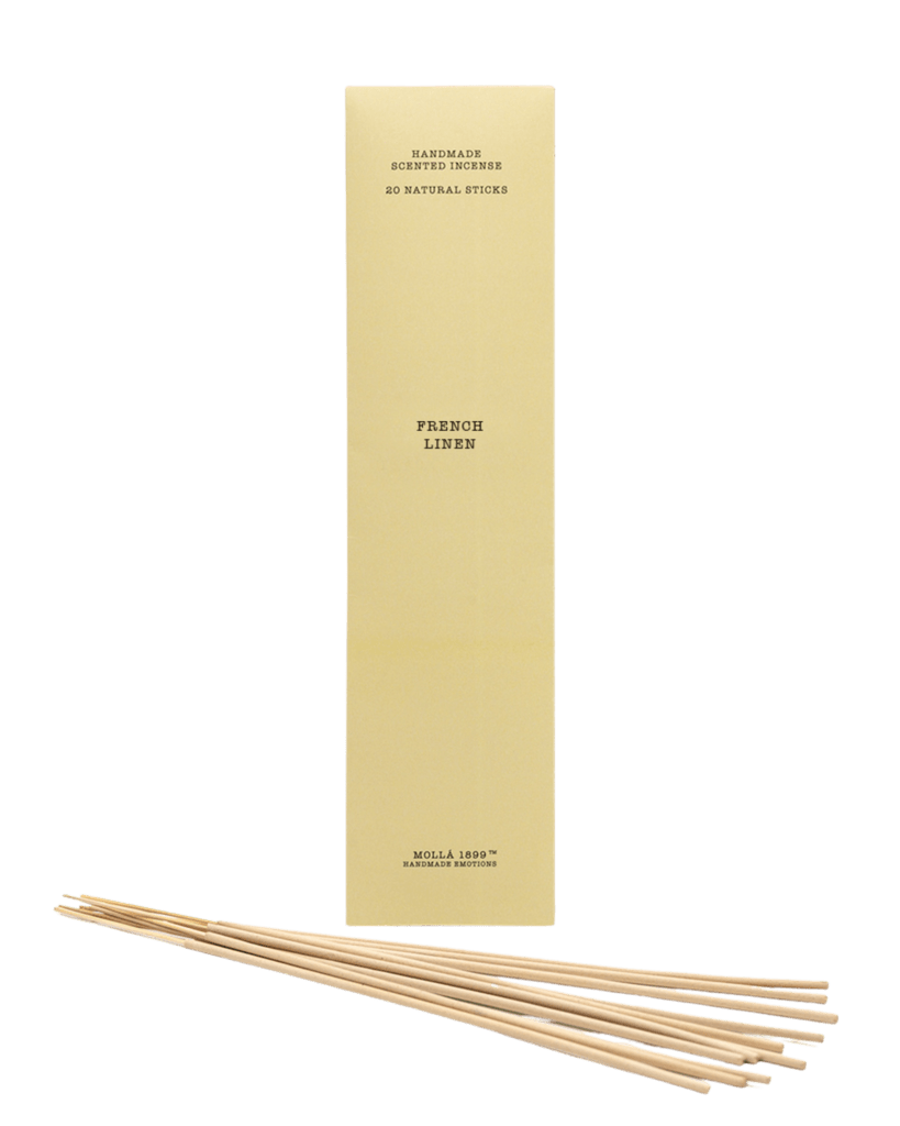 A tall, beige box labeled Cereria Molla - French Linen Incense 20pk stands upright, emitting a gentle fragrance. Several natural incense sticks are arranged in front on a plain surface. The box features text indicating Handmade Scented Incense and 20 Natural Sticks.