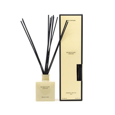 The Cereria Molla Moroccan Cedar 3.4oz Reed Diffuser features a square beige bottle with black reeds, accompanied by an upright beige and black box that’s partially open to reveal the cedar wood fragrance.