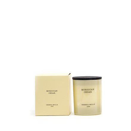 The Cereria Molla - Moroccan Cedar 8oz Candle, crafted from vegetable wax, features a cream hue and a black lid, accompanied by a matching box. Both items showcase minimal black text, embodying simplicity and elegance in refined scented candle design.