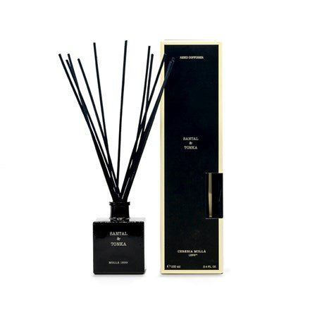 The Cereria Molla - Santal & Tonka 3.4oz Reed Diffuser includes a rectangular black bottle labeled with Cedar Oil, complemented by thin black reeds and a matching black box with golden edges.