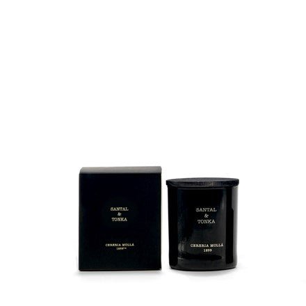 A black glass Cereria Molla - Santal & Tonka 8oz Candle, featuring gold lettering, sits beside its matching box on a white background. This handmade piece embodies elegance and sophistication.