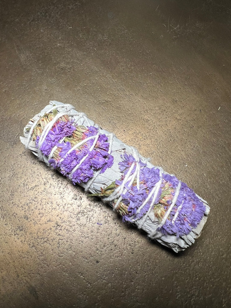 A 4 Purple Daze Sage bundle by Designs by Deekay, wrapped with white string and featuring sage leaves beneath layers of lavender, lies on a dark surface, ready to cleanse and purify with an aura of tranquility.