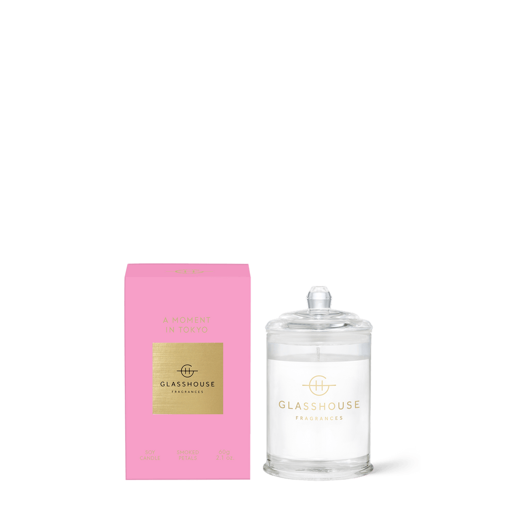 A Glasshouse Fragrances - A Moment In Tokyo pink box is next to a clear candle jar. This triple-scented, natural soy wax candle captures the Tokyo Smoked Petals essence.