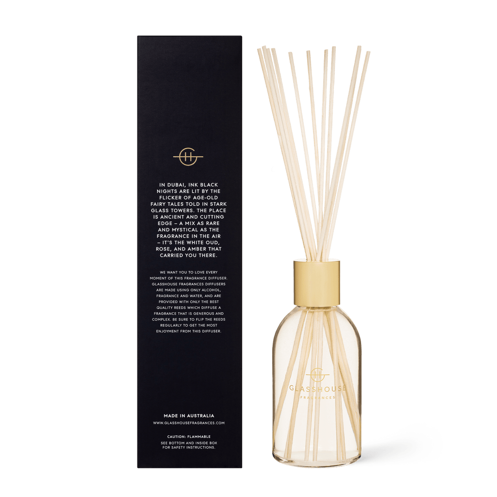 A Glasshouse Fragrances diffuser, Arabian Nights edition, features a sleek glass bottle with reeds and a black rectangular box. The label highlights scents of saffron, rich amber, rose, and white oud.