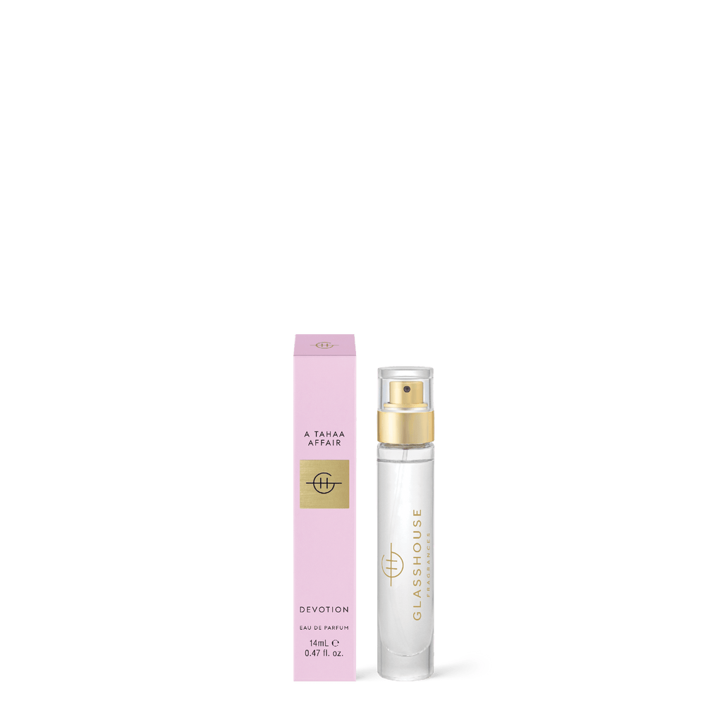 The minimalist design of a clear glass perfume bottle with a gold spray top labeled Glasshouse Fragrances is next to a pink box labeled A Tahaa Affair Devotion Eau de Parfum 14ml. The fragrance blends jasmine and butterscotch caramel notes.