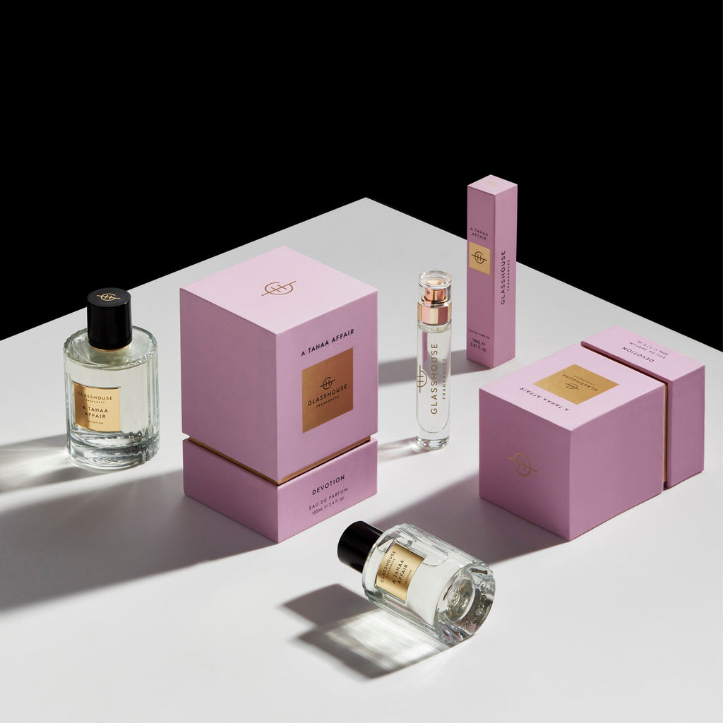 Glasshouse Fragrances A Tahaa Affair Eau de Parfum 14ml, showcased in clear bottles and elegant pink boxes, sits on a white surface against a black background.