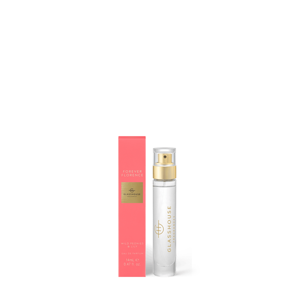 The Forever Florence Eau de Parfum 14ml by Glasshouse Fragrances features a transparent bottle with a gold nozzle beside its pink coral box adorned with golden text, capturing enchanting notes of lily and peonies.