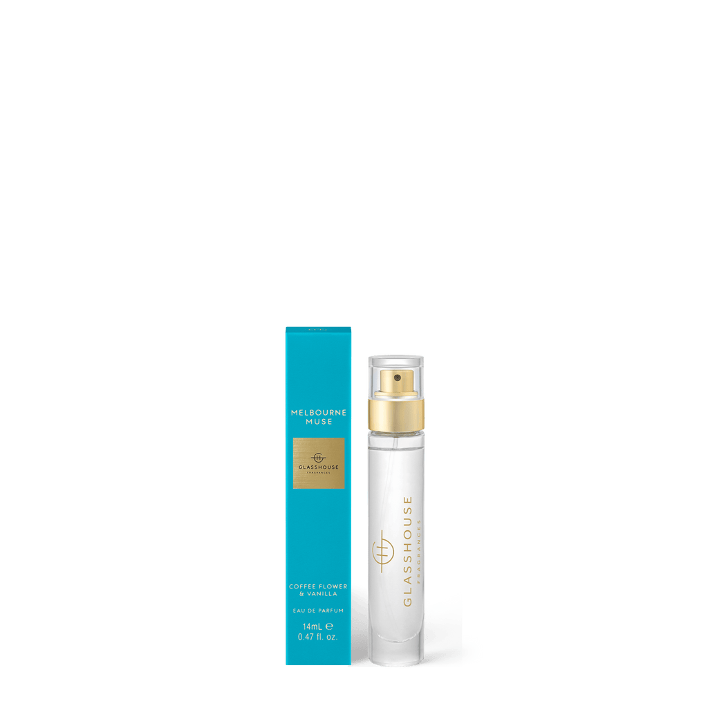 A clear Glasshouse Fragrances perfume bottle, labeled Melbourne Muse, stands beside a tall, teal box. The bottle features a gold spray cap and contains a light-colored liquid with notes of orange blossom and vanilla.