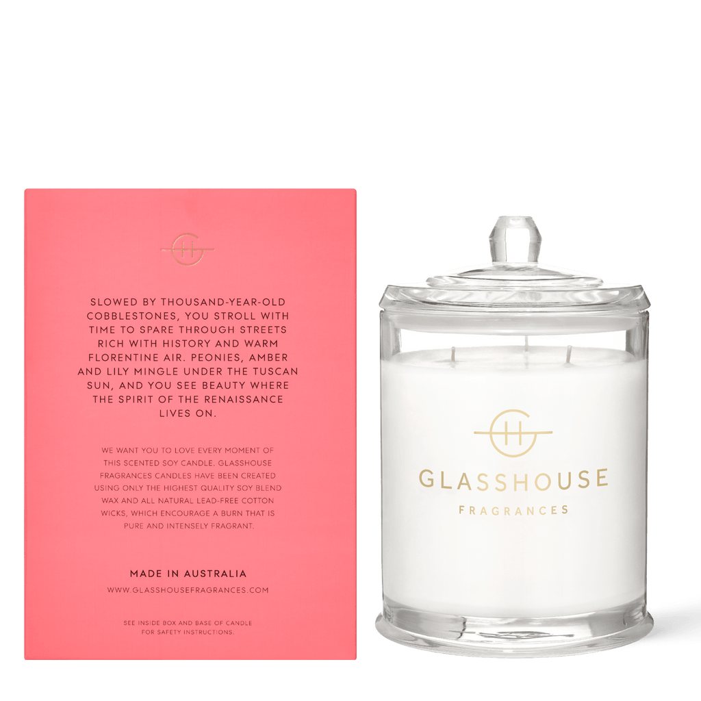 A Glasshouse Fragrances - Forever Florence Candle 760g, housed in glass with a lid, stands next to a pink box detailing its origins and peony-lily scents. Made in Australia is visible at the bottom.