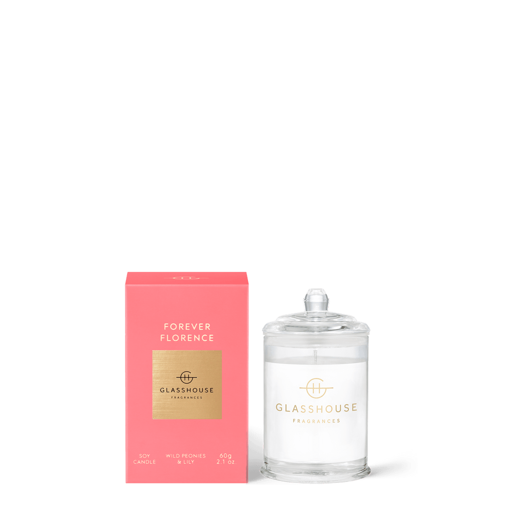 A Glasshouse Fragrances - Forever Florence Mini soy candle is shown with its pink and gold box. The clear glass jar has a lid, and the candle features a triple-scented aroma of wild peonies and lily with natural lead-free cotton wicks.