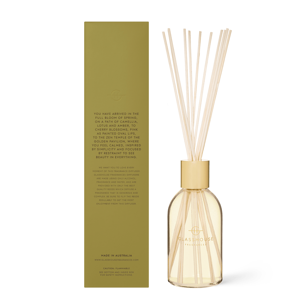 The Kyoto in Bloom Diffuser by Glasshouse Fragrances showcases thin reed sticks in a clear, rounded glass bottle and comes in an elegant gold box with the brand logo. It offers hints of camellia and lotus for a delightful aromatic experience.