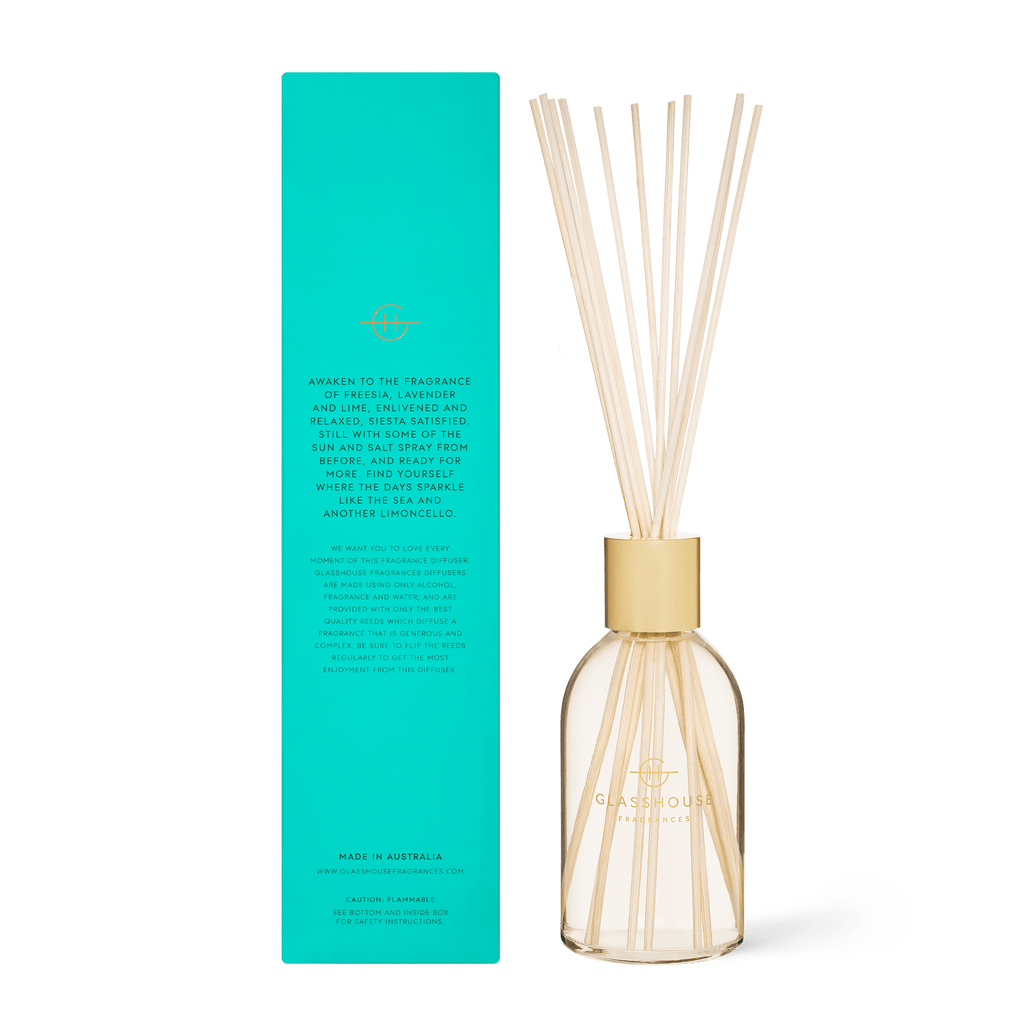 The Lost in Amalfi Diffuser features a clear, non-toxic glass bottle with gold text and the Glasshouse Fragrances logo. It stands next to a tall green box with cursive writing and the brands logo, complete with reed sticks.