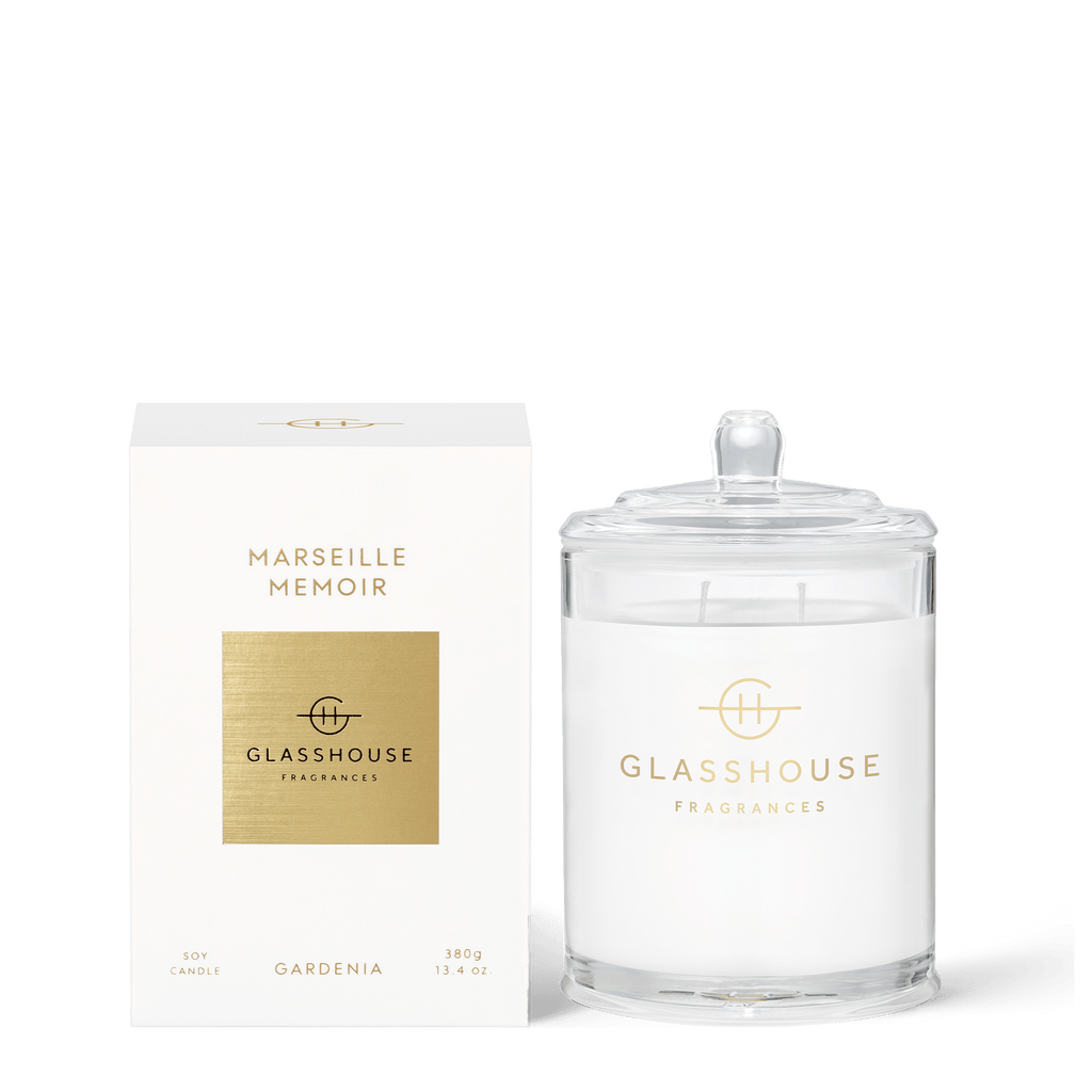 The Glasshouse Fragrances - Marseille Memoir 13.4oz candle, a white cylindrical triple-scented soy candle with gardenia and neroli notes, comes in a clear glass jar with a lid and is paired with matching white and gold packaging.