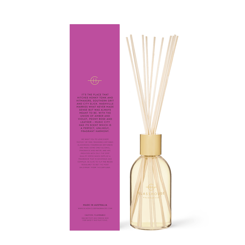 The Glasshouse Fragrances - Music City Magic Diffuser, featuring a glass bottle with light wooden reeds beside its pink box, both featuring minimalist branding, exudes sophistication. The peony rose scent enhances the ensembles elegance with floral luxury.