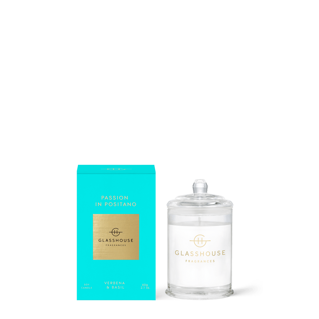 A clear glass candle with a lid labeled Glasshouse Fragrances sits next to a turquoise box labeled Passion in Positano, capturing the essence of an Italian Citrus Bouquet with verbena and basil notes, representing the Glasshouse Fragrances - Passion In Positano Mini 2.1oz Candle.