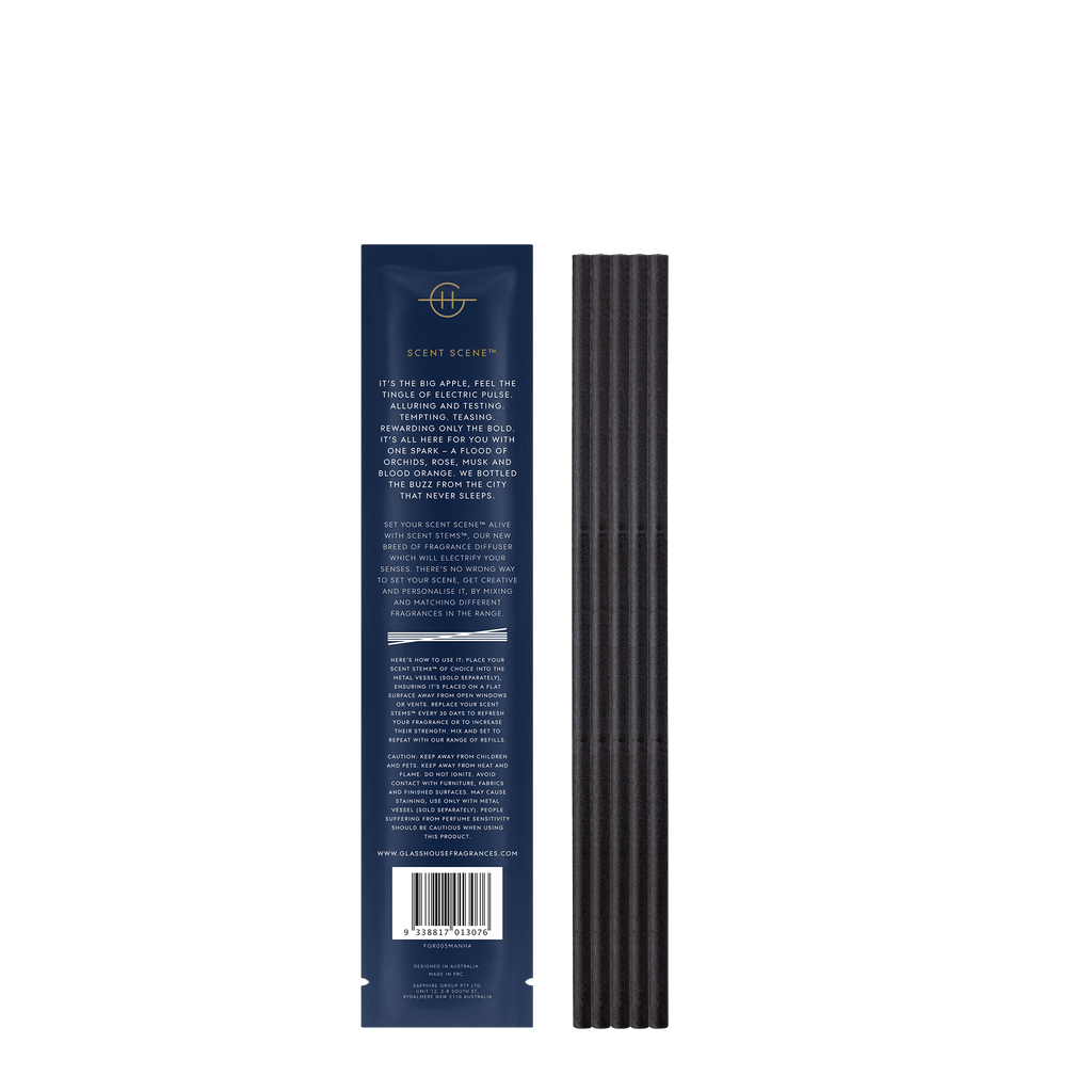 A dark blue rectangular package with gold branding, white text, and a hint of blood orange, sits next to vertically aligned black scent stems from Glasshouse Fragrances Ill Take Manhattan. A barcode is on the bottom.