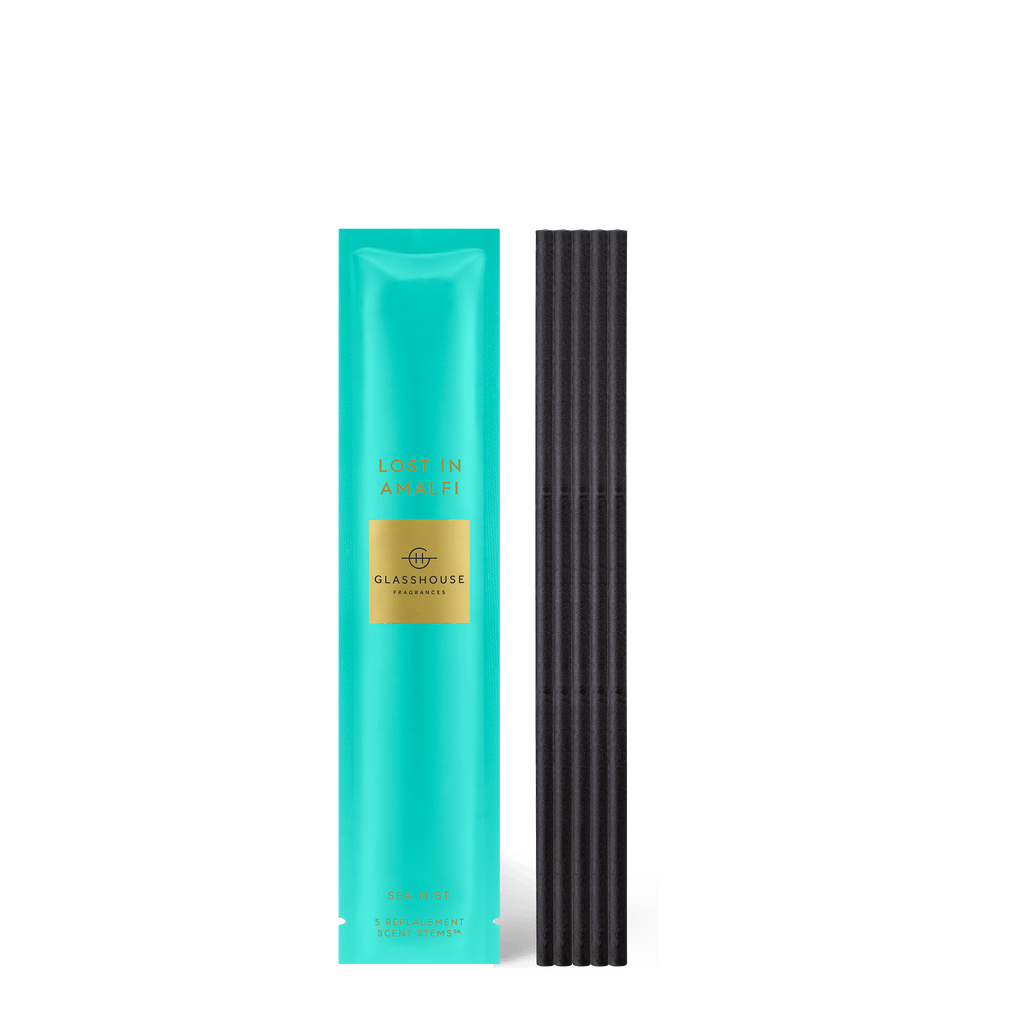 A turquoise box labeled Lost in Amalfi and featuring a gold rectangle sits beside black ribbed diffuser reeds. This product, designed for the SEA MIST fragrance experience, is named Glasshouse Fragrances - Replacement Scent Stems - Lost In Amalfi.