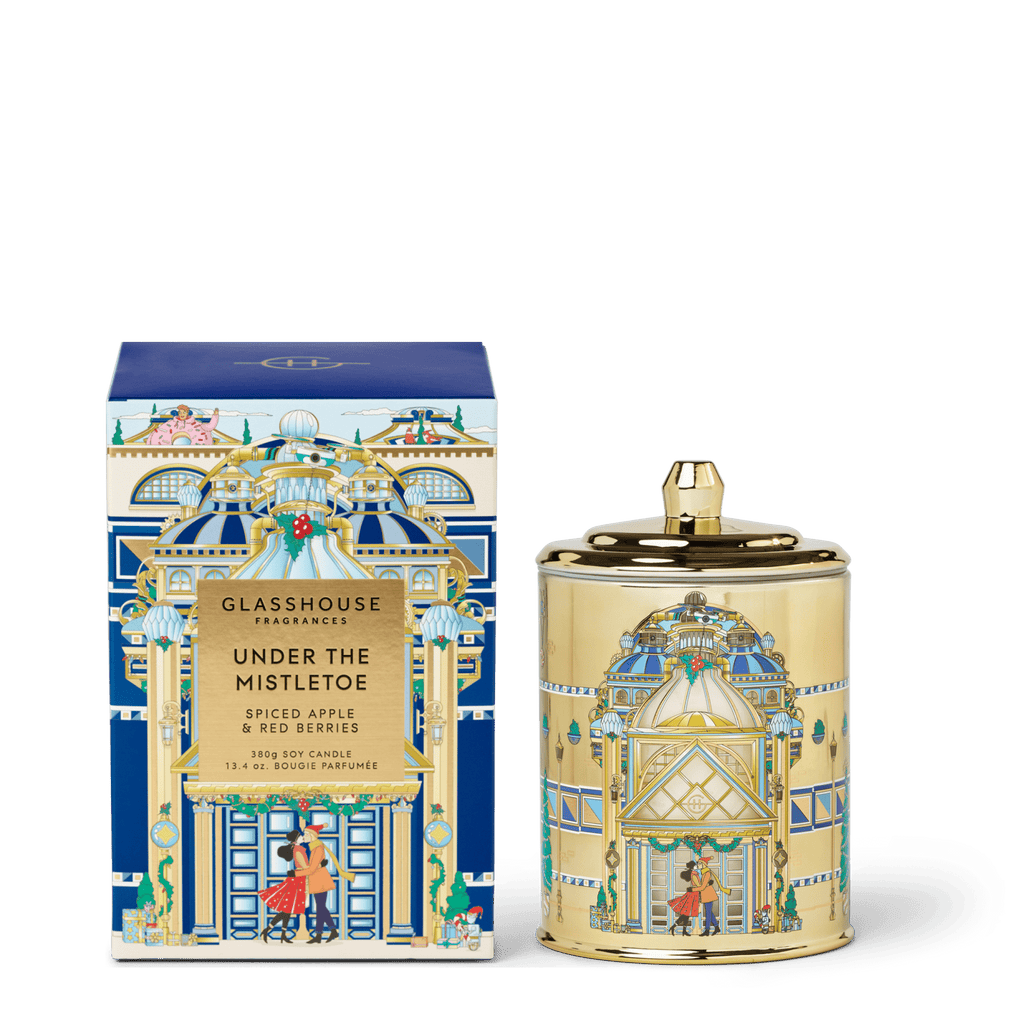 The Glasshouse Fragrances - Under the Mistletoe Candle comes in a decorative box featuring a festive architectural design with a couple under mistletoe and has a Spiced Apple & Red Berries scent.