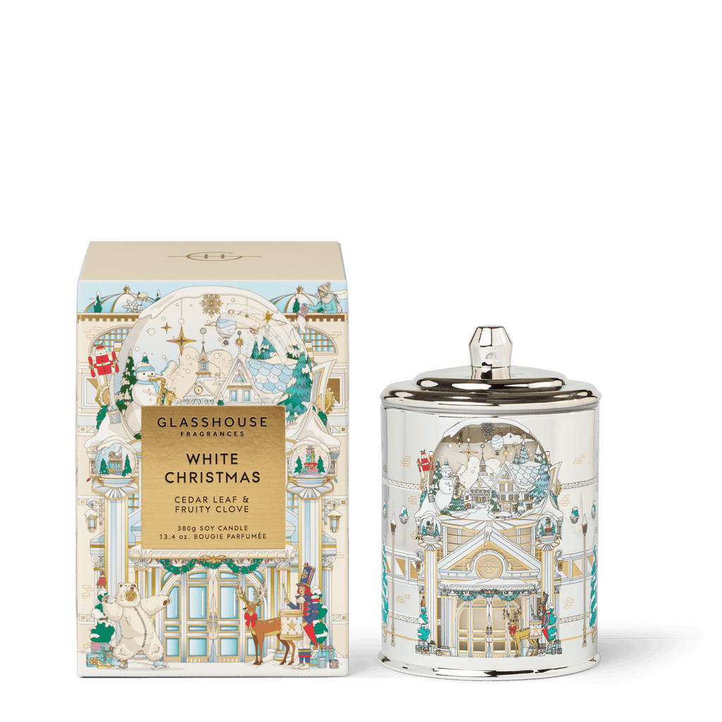 The Glasshouse Fragrances - White Christmas 13.4oz Candle features festive packaging with pastel Christmas scenes and is crafted from a premium soy blend wax. Both box and jar show decorated buildings and polar bears.