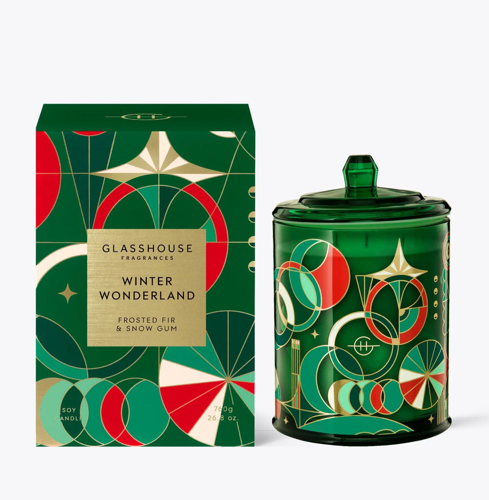 A 26.8oz green soy blend wax candle from Glasshouse Fragrances comes in a geometric holiday-themed box in red, white, and gold. Labeled Winter Wonderland, Frosted Fir & Snow Gum, it features a lid with a pointed handle.