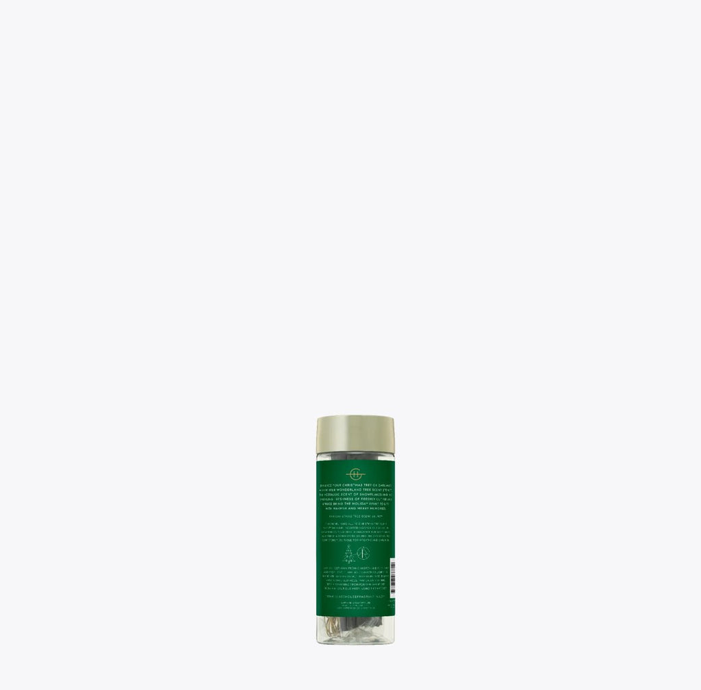 A small, transparent, green Glasshouse Fragrances bottle with a beige cap displays text and symbols on its label. It stands upright against a white backdrop, revealing the Spruce scent of Winter Wonderland Tree Hanging Scent Stems, evoking the refreshing aroma of Fir Balsam forests.