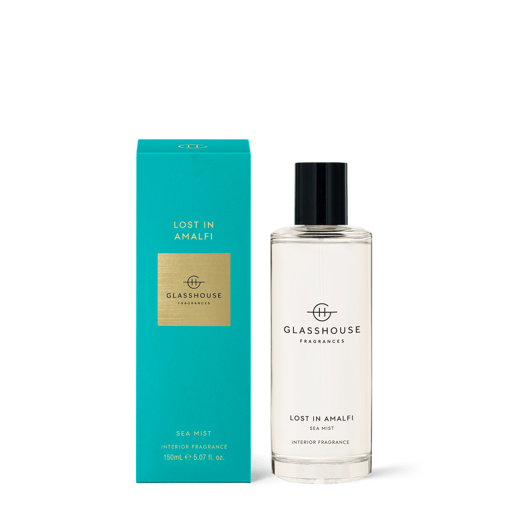 The Glasshouse - Lost in Amalfi Room Spray is showcased with its matching turquoise box. The clear bottle, enriched with freesia notes, features a black cap and the Glasshouse Fragrances branding elegantly printed in black on both pieces.