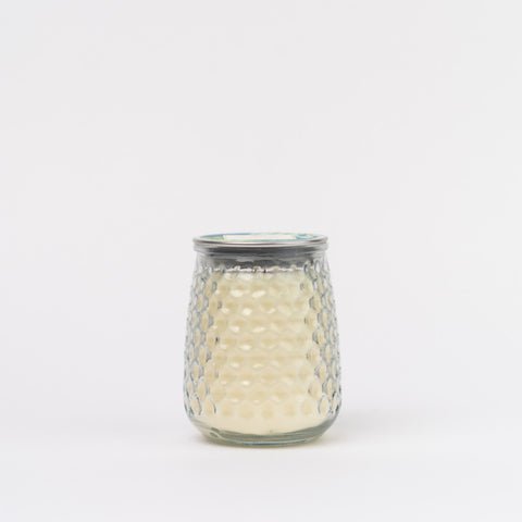 A Spa Springs Signature Candle by Greenleaf features a glass jar with a textured honeycomb design filled with creamy white wax, topped with a metal lid, and set against a plain white background, capturing serene essence.