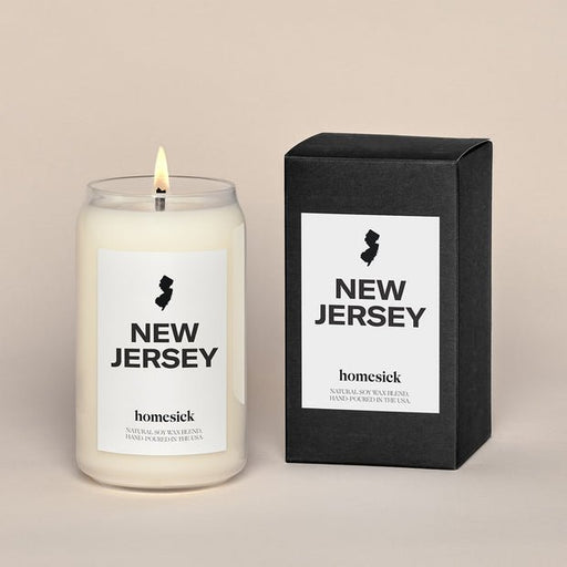 A Homesick - New Jersey Candle in a glass jar is beside a matching black box, both featuring state silhouettes. These natural soy wax candles are infused with fragrance oils and highlight Homesick branding, emphasizing hand-pouring in the USA.