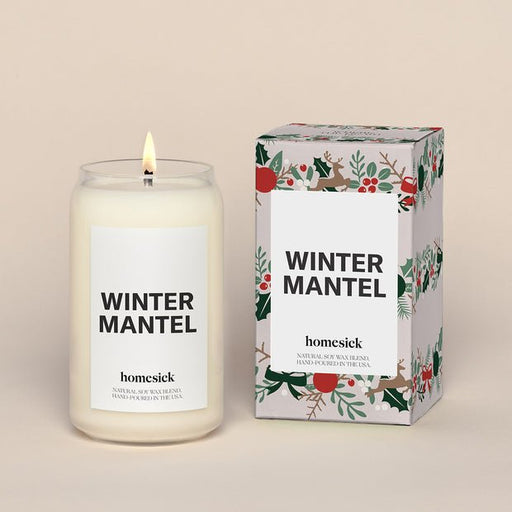 The Homesick - Winter Mantel Candle sits lit beside its decorative box, both crafted from a soothing soy wax blend. The box showcases a festive floral design in red and green, with the Homesick brand name displayed on both items.