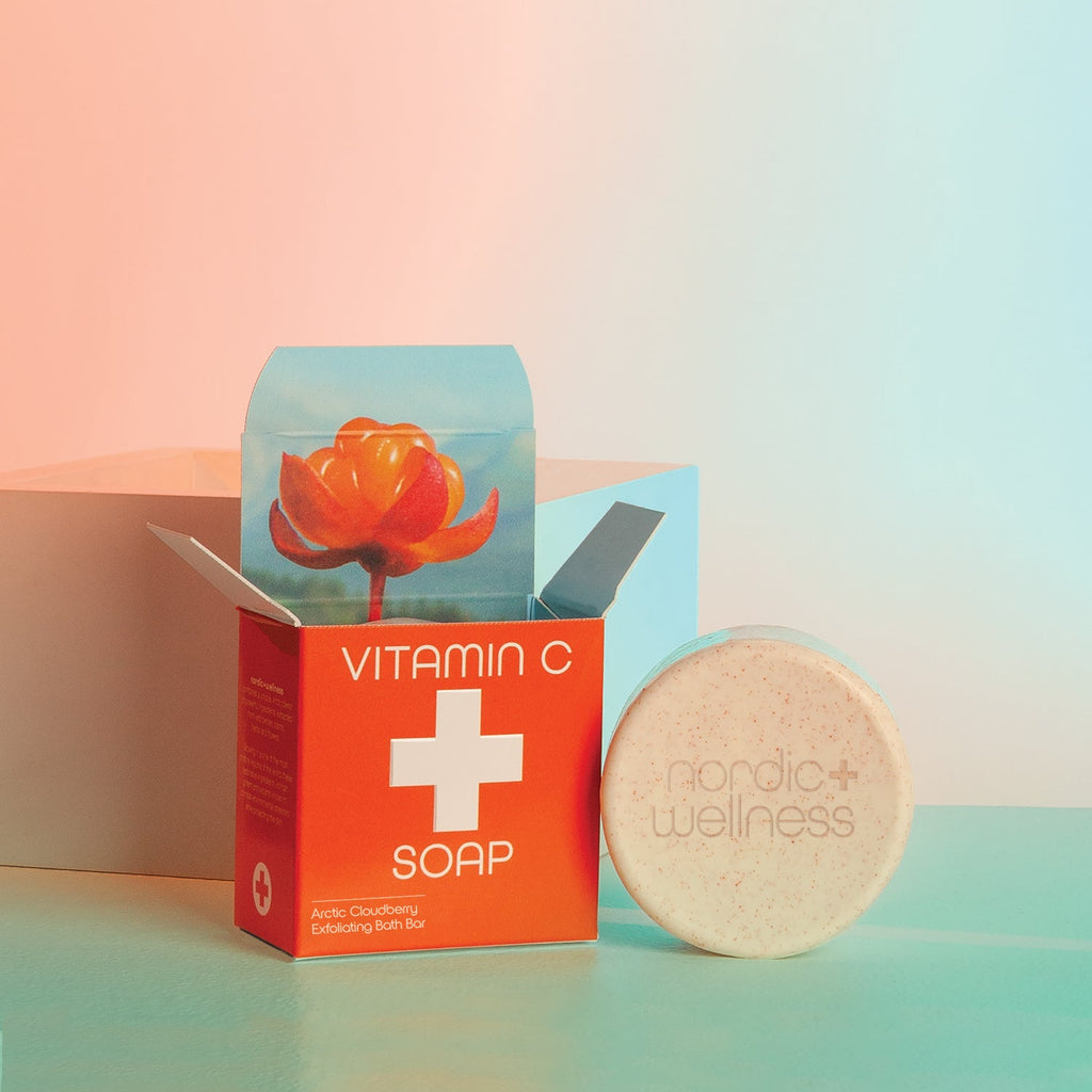 An open bright red box labeled Kalastyle - Nordic+Wellness Vitamin C Soap Bar displays a vibrant orange flower and Arctic cloudberry extract. Beside it sits a round, creamy soap bar embossed with the Nordic Wellness logo, set against a pastel background.