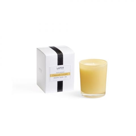 A yellow candle in a clear holder is next to a white box with black stripes labeled Lafco and Chamomile Lavender. The soothing chamomile and lavender scents are highlighted against a plain white background.