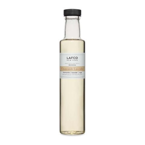 The Lafco Chamomile Lavender 8.4oz Diffuser Refill features a tall glass bottle with a black cap and clear label detailing the scent. The light yellow liquid is infused with calming Chamomile and soothing Lavender.