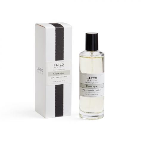 A bottle of Lafco - Champagne Room Mist, known for its luxury fragrance, sits beside its white box with a black vertical stripe. The simple, elegant label and black cap reflect the sophistication of this Lafco product.