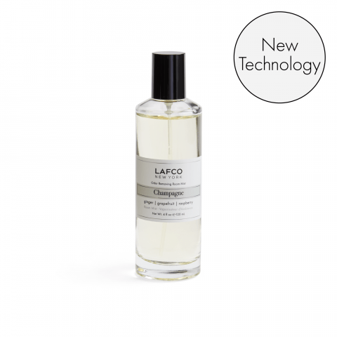 A clear bottle of Lafco - Champagne Room Mist with a black cap and white label is displayed on a white background. A circular badge reads New Technology. Enjoy this luxurious fragrance and odor-removing formula for your home.