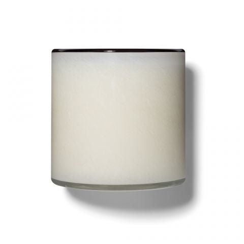 The Lafco - Champagne Signature 15.5oz Candle emits a soft champagne hue with a frosted glass design, casting a subtle shadow on its white surroundings. The sleek, modern aesthetic is highlighted by a dark rim on top.